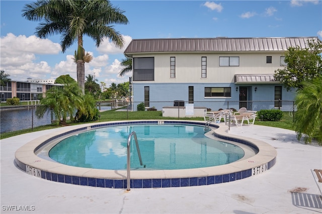pool featuring a patio, a water view, and fence