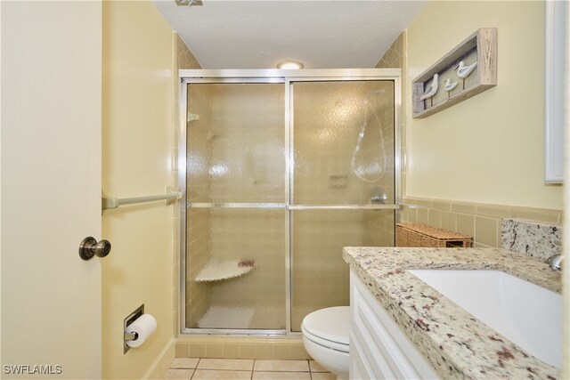 bathroom with toilet, tile walls, vanity, a shower with door, and tile patterned flooring