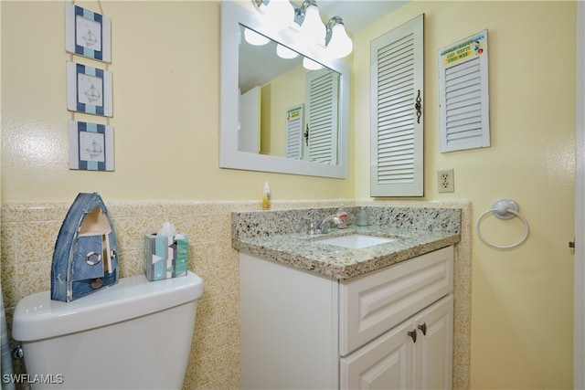 bathroom featuring tile walls, toilet, vanity, and wainscoting