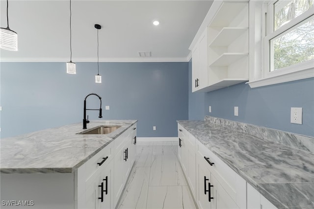 kitchen featuring sink, an island with sink, white cabinetry, decorative light fixtures, and light stone counters