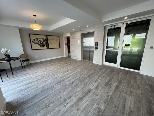 unfurnished living room with a tray ceiling, elevator, and hardwood / wood-style flooring