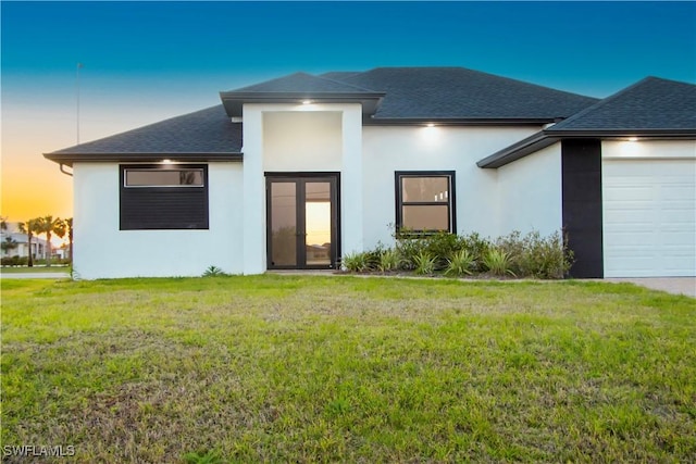 view of front facade featuring a front lawn, roof with shingles, an attached garage, and stucco siding