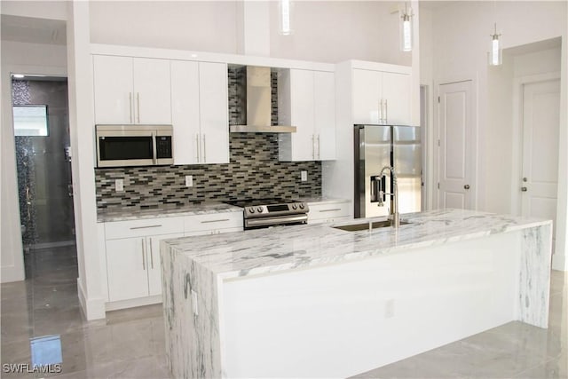 kitchen with decorative backsplash, an island with sink, wall chimney exhaust hood, appliances with stainless steel finishes, and white cabinetry