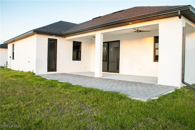 back of house with a yard, roof with shingles, a patio, and stucco siding