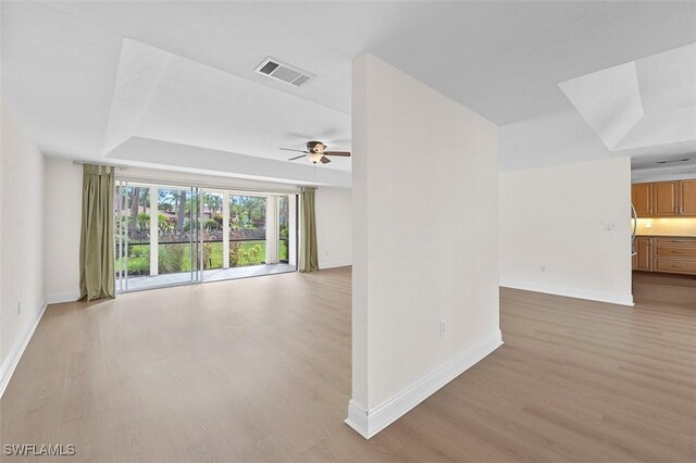 unfurnished room featuring ceiling fan, a tray ceiling, and light hardwood / wood-style flooring