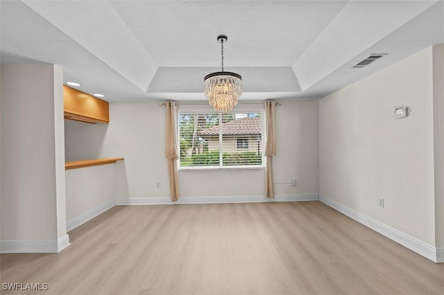 unfurnished dining area with a tray ceiling, light wood-type flooring, visible vents, and baseboards