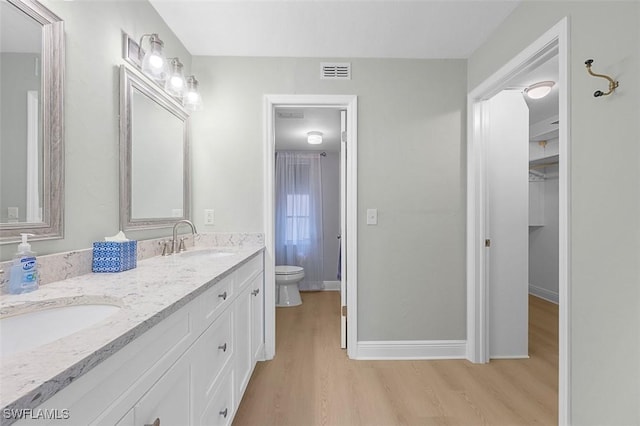 full bathroom featuring toilet, wood finished floors, a sink, visible vents, and baseboards