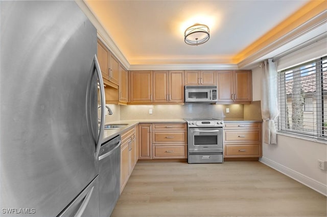 kitchen with stainless steel appliances, a sink, baseboards, light countertops, and light wood-type flooring