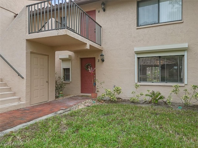 entrance to property featuring a yard, a balcony, and stucco siding