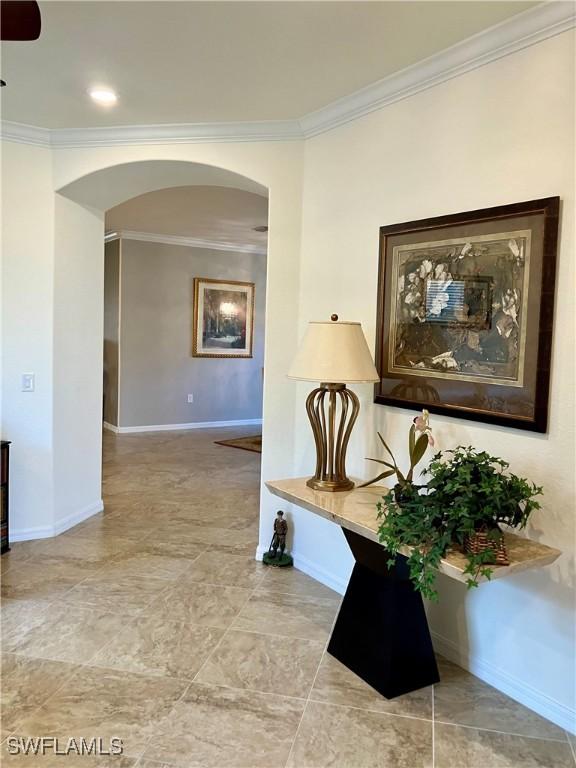 hallway with arched walkways, crown molding, and baseboards