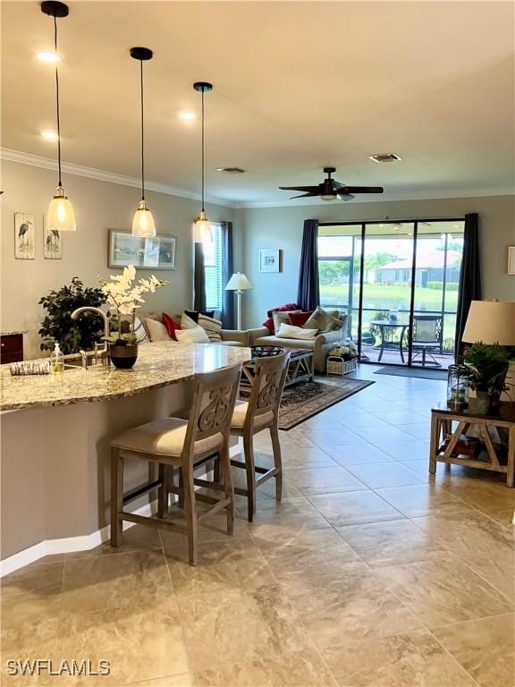 kitchen with a kitchen breakfast bar, crown molding, ceiling fan, decorative light fixtures, and light stone counters