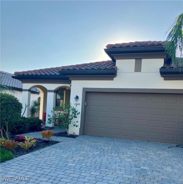 mediterranean / spanish home with a garage, a tiled roof, decorative driveway, and stucco siding