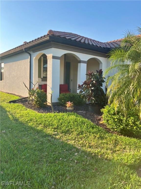 view of side of property with a yard, a tiled roof, and stucco siding