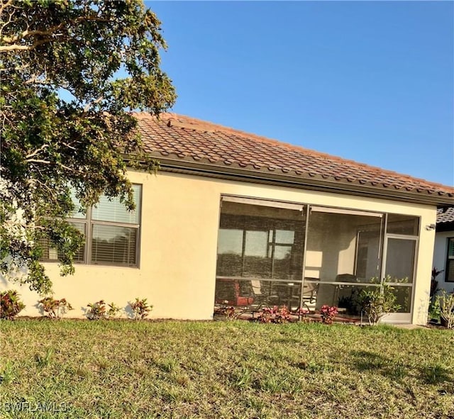 back of house featuring a sunroom, a yard, a tiled roof, and stucco siding