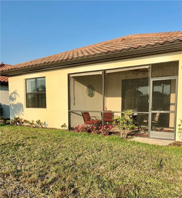 back of house with a yard, stucco siding, a sunroom, and a tiled roof