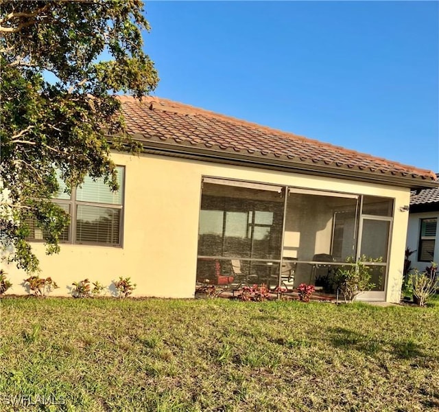 view of property exterior featuring a yard, a tile roof, a sunroom, and stucco siding