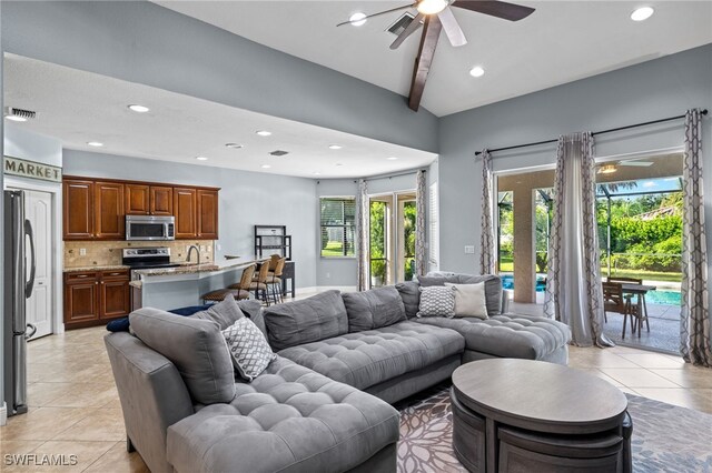 living room featuring beam ceiling, sink, ceiling fan, and light tile patterned floors