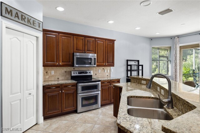 kitchen featuring sink, appliances with stainless steel finishes, light stone counters, tasteful backsplash, and light tile patterned flooring