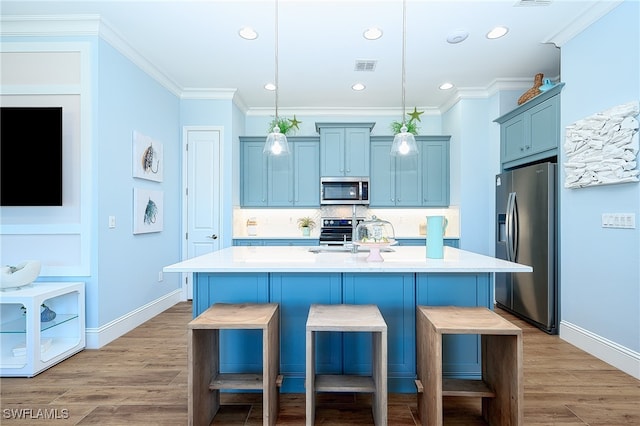 kitchen with a breakfast bar, stainless steel appliances, pendant lighting, light hardwood / wood-style flooring, and a kitchen island with sink