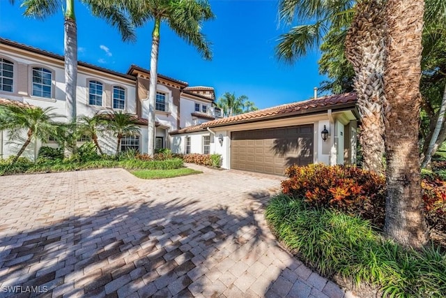 mediterranean / spanish house with a tile roof, decorative driveway, a garage, and stucco siding