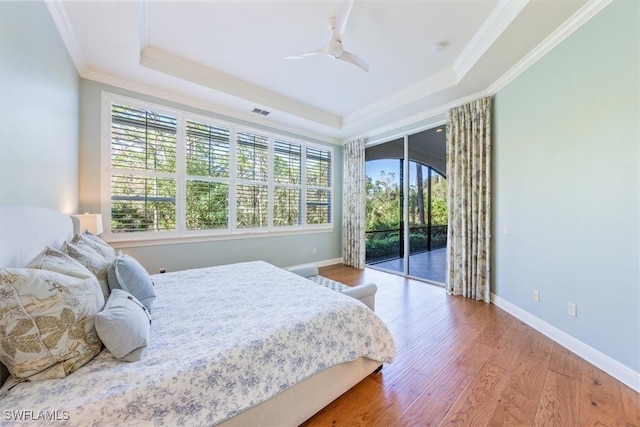 bedroom with a raised ceiling, access to exterior, ornamental molding, hardwood / wood-style flooring, and ceiling fan