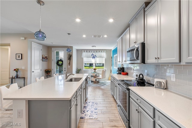 kitchen with sink, a breakfast bar, appliances with stainless steel finishes, hanging light fixtures, and light wood-type flooring