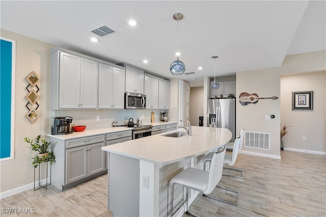 kitchen with stainless steel appliances, sink, decorative light fixtures, an island with sink, and light wood-type flooring