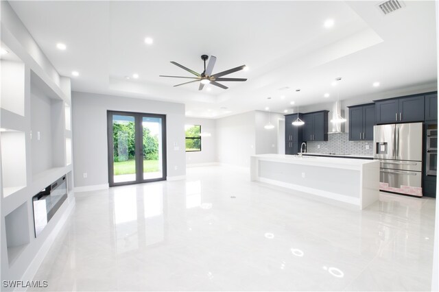 kitchen featuring a kitchen island with sink, sink, ceiling fan, stainless steel refrigerator with ice dispenser, and a raised ceiling