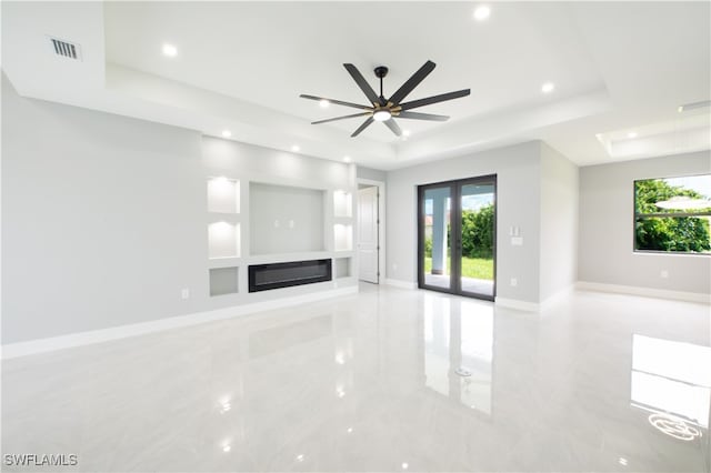 unfurnished living room featuring a tray ceiling, a healthy amount of sunlight, and ceiling fan