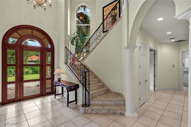 entryway with light tile patterned floors, a chandelier, ornate columns, and a high ceiling