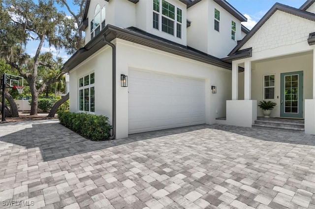 view of side of property with stucco siding, an attached garage, and decorative driveway