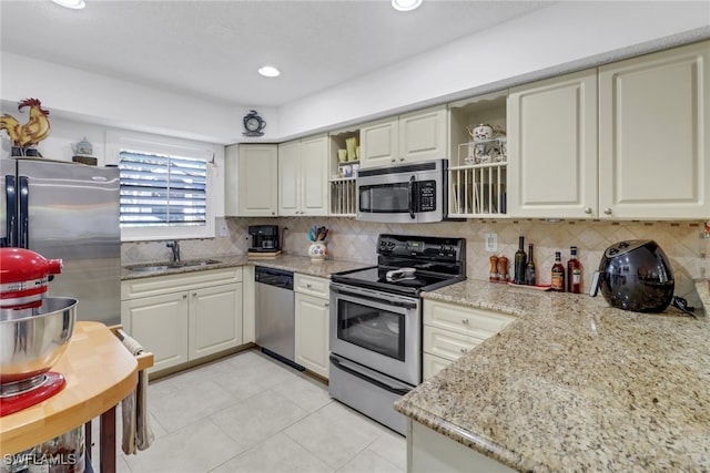 kitchen with backsplash, light tile patterned floors, appliances with stainless steel finishes, light stone countertops, and sink