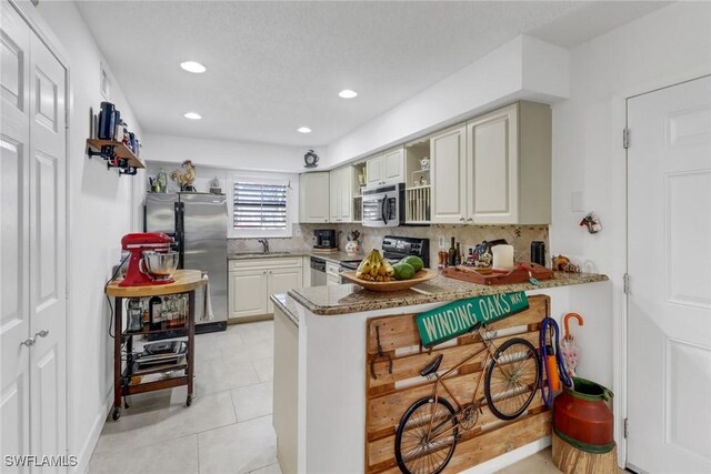 kitchen featuring dark stone counters, light tile patterned floors, kitchen peninsula, decorative backsplash, and appliances with stainless steel finishes