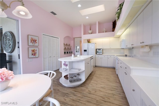 kitchen with a skylight, white cabinetry, decorative light fixtures, a kitchen island, and light wood-type flooring