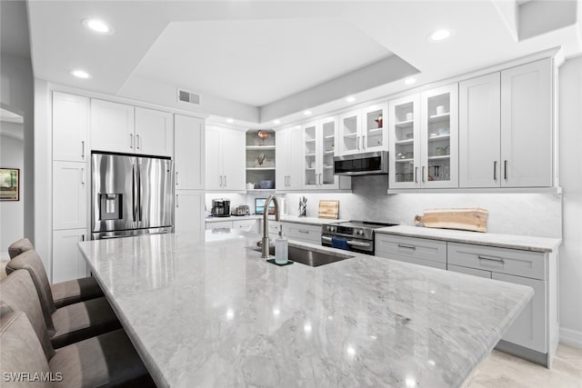 kitchen with light stone counters, white cabinets, sink, appliances with stainless steel finishes, and a kitchen bar