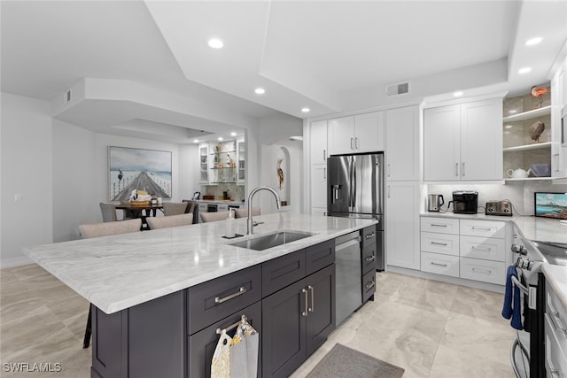 kitchen featuring sink, an island with sink, white cabinets, appliances with stainless steel finishes, and a kitchen bar