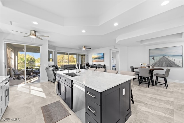 kitchen featuring an island with sink, sink, dishwasher, a tray ceiling, and a kitchen breakfast bar