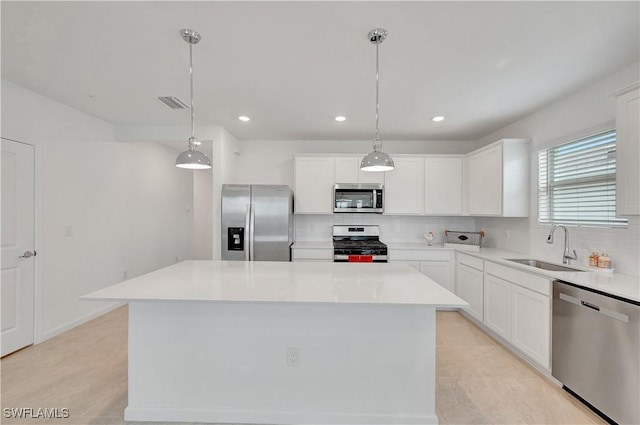 kitchen with white cabinets, appliances with stainless steel finishes, a kitchen island, sink, and hanging light fixtures