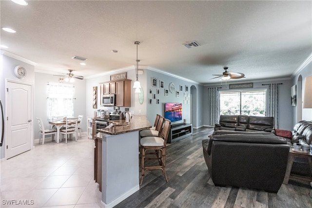 kitchen with a kitchen breakfast bar, kitchen peninsula, ceiling fan, hanging light fixtures, and appliances with stainless steel finishes