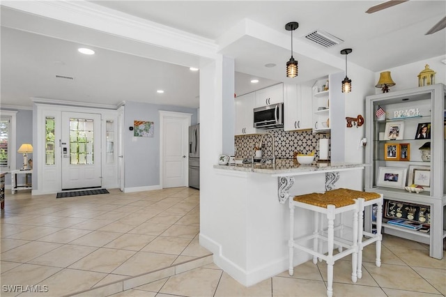 kitchen with a breakfast bar area, stainless steel appliances, white cabinets, light tile patterned flooring, and kitchen peninsula