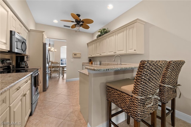 kitchen with ceiling fan with notable chandelier, appliances with stainless steel finishes, light stone counters, and a breakfast bar