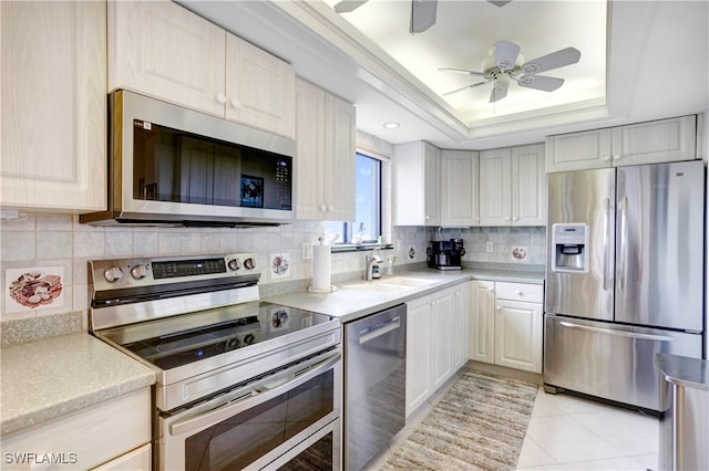 kitchen featuring appliances with stainless steel finishes, a raised ceiling, sink, and ceiling fan