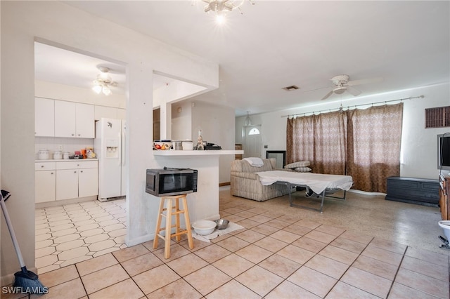 kitchen with white cabinets, ceiling fan, a kitchen bar, and white refrigerator with ice dispenser