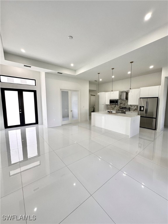 kitchen featuring white cabinets, french doors, stainless steel appliances, pendant lighting, and a kitchen island with sink