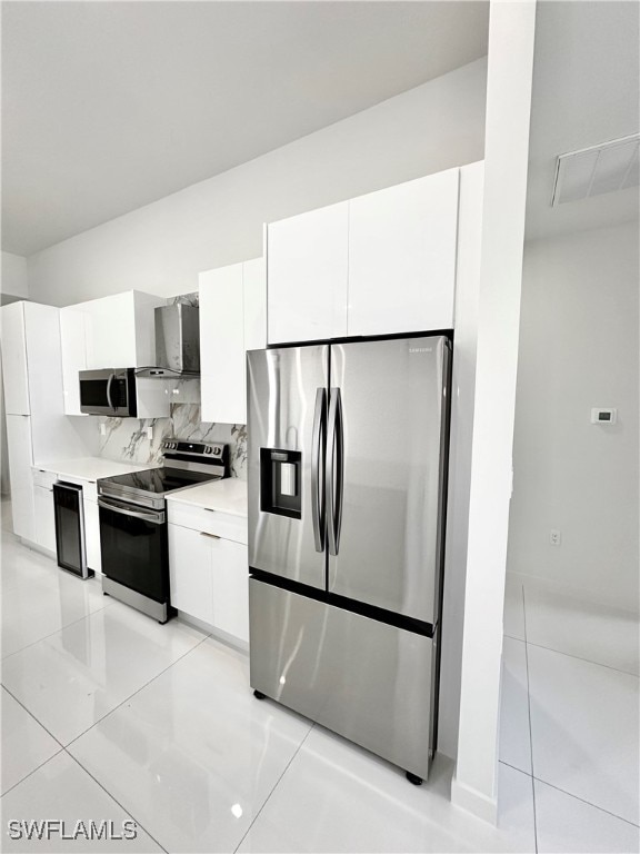 kitchen featuring stainless steel appliances, light tile patterned floors, white cabinets, and tasteful backsplash