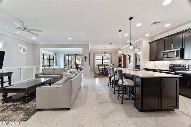 kitchen with an island with sink, ornamental molding, ceiling fan, and stainless steel appliances