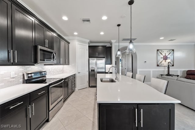 kitchen featuring appliances with stainless steel finishes, backsplash, pendant lighting, a center island with sink, and sink