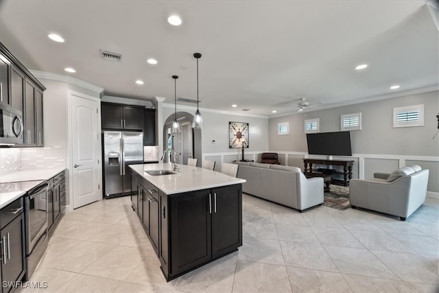 kitchen with tasteful backsplash, a center island with sink, appliances with stainless steel finishes, decorative light fixtures, and ceiling fan