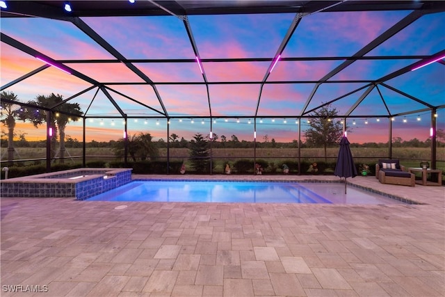 pool at dusk with an in ground hot tub, glass enclosure, and a patio area