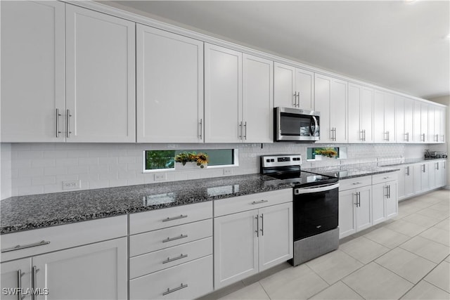 kitchen with dark stone counters, white cabinets, stainless steel appliances, and light tile patterned floors